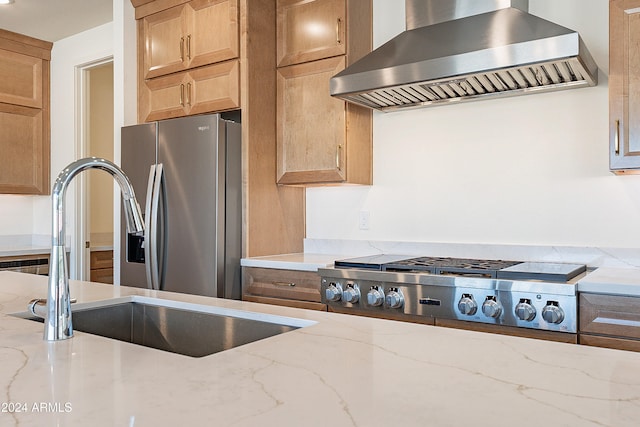 kitchen with light stone counters, sink, wall chimney range hood, and appliances with stainless steel finishes