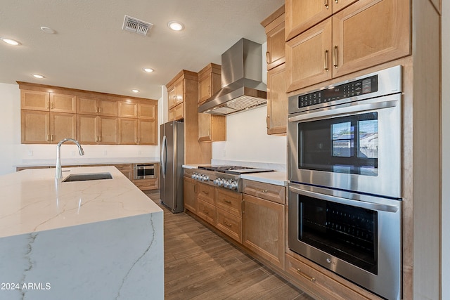 kitchen featuring appliances with stainless steel finishes, light stone counters, sink, wall chimney range hood, and hardwood / wood-style floors