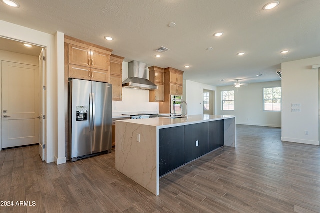 kitchen with light brown cabinets, a kitchen island with sink, wall chimney exhaust hood, dark hardwood / wood-style floors, and stainless steel fridge with ice dispenser