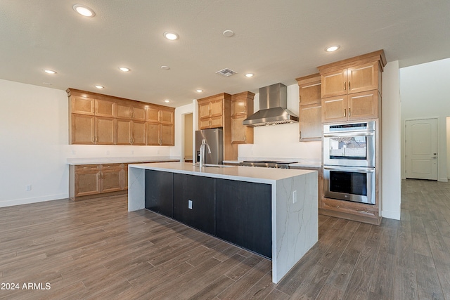 kitchen with sink, wall chimney exhaust hood, stainless steel appliances, dark hardwood / wood-style floors, and a kitchen island with sink