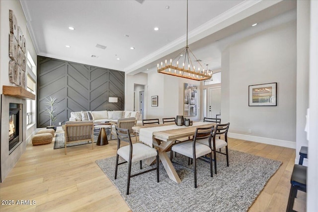 dining area with a large fireplace, light wood-type flooring, crown molding, and a chandelier