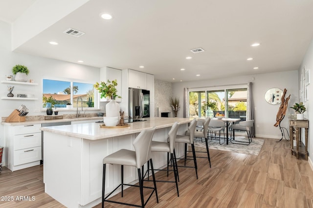 kitchen with stainless steel refrigerator with ice dispenser, white cabinets, a breakfast bar, and a center island