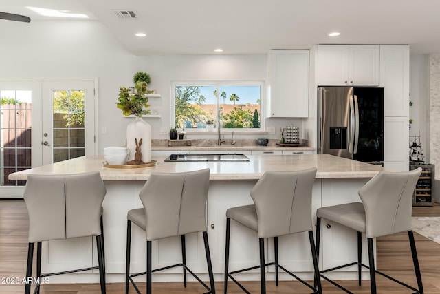 kitchen with stainless steel refrigerator with ice dispenser, a breakfast bar, white cabinets, and a kitchen island