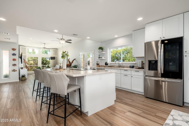 kitchen featuring a kitchen island, a kitchen bar, white cabinetry, stainless steel fridge with ice dispenser, and light wood-type flooring