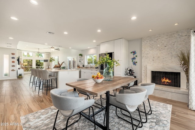 dining space with ceiling fan, a healthy amount of sunlight, a fireplace, and light hardwood / wood-style floors