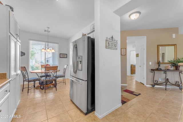 kitchen with an inviting chandelier, light tile patterned floors, stainless steel fridge, pendant lighting, and white cabinets