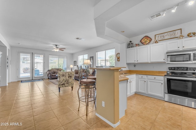 kitchen featuring light tile patterned floors, appliances with stainless steel finishes, white cabinets, a kitchen bar, and kitchen peninsula