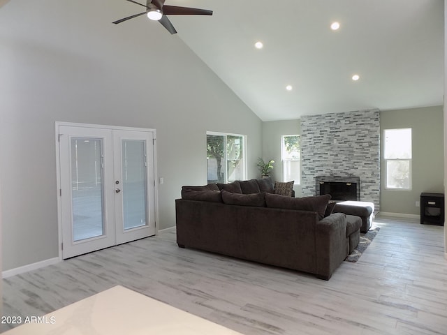 living room featuring ceiling fan, light hardwood / wood-style floors, high vaulted ceiling, a tile fireplace, and french doors