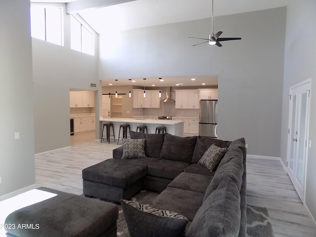 living room with light wood-type flooring, ceiling fan, beam ceiling, sink, and high vaulted ceiling