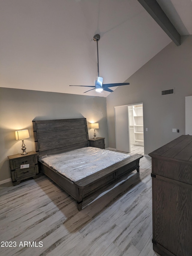 bedroom featuring beam ceiling, a spacious closet, ceiling fan, and light wood-type flooring