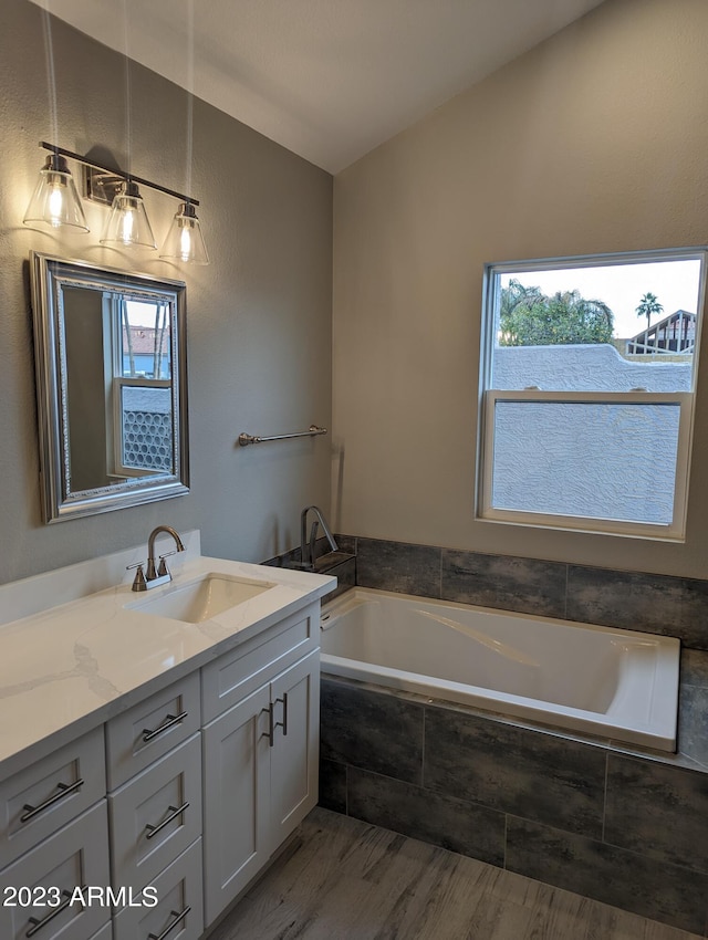 bathroom with a relaxing tiled bath, vanity, and wood-type flooring