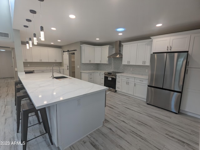 kitchen with hanging light fixtures, stainless steel appliances, light hardwood / wood-style flooring, and wall chimney exhaust hood