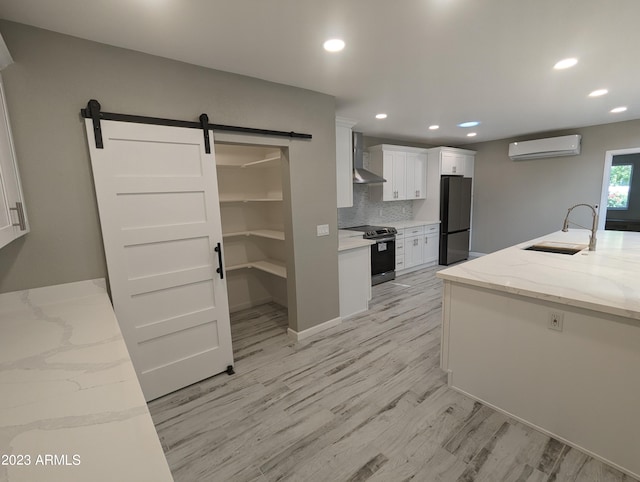 kitchen with an AC wall unit, appliances with stainless steel finishes, a barn door, white cabinetry, and light hardwood / wood-style flooring