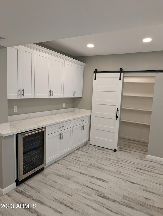 kitchen with a barn door, light stone countertops, wine cooler, white cabinets, and light wood-type flooring