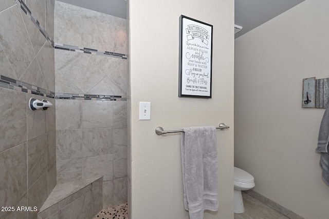 full bath featuring a tile shower, toilet, and baseboards