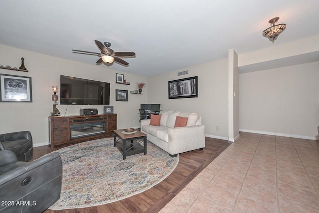 living room featuring tile patterned floors, visible vents, baseboards, and ceiling fan