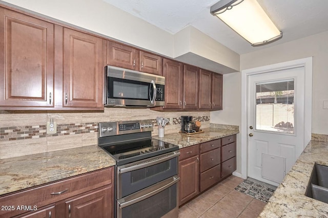 kitchen featuring a sink, tasteful backsplash, appliances with stainless steel finishes, light tile patterned floors, and light stone countertops