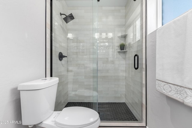 bathroom featuring a shower with door and toilet