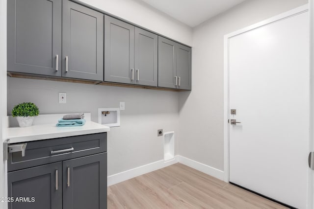 clothes washing area with washer hookup, electric dryer hookup, light hardwood / wood-style flooring, and cabinets