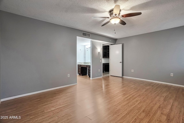 empty room with light wood-style flooring, a ceiling fan, visible vents, and baseboards