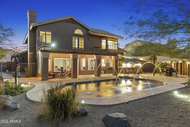 back house at dusk with a patio, pool water feature, and a balcony