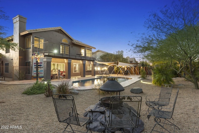 back house at dusk with a fenced in pool, a patio, a balcony, and pool water feature