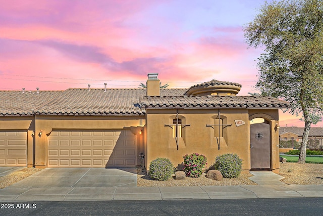 view of front facade with a tile roof, a chimney, stucco siding, an attached garage, and driveway