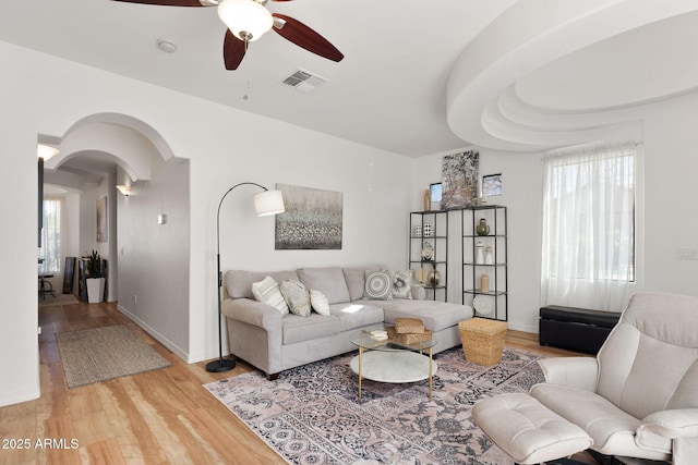 living area featuring arched walkways, visible vents, a ceiling fan, wood finished floors, and baseboards