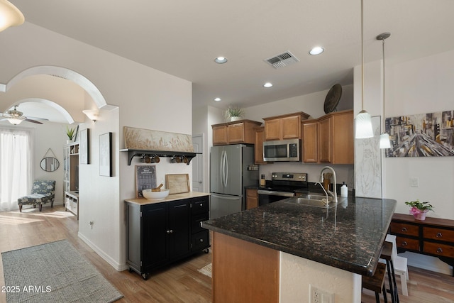 kitchen featuring stainless steel appliances, a peninsula, a sink, visible vents, and decorative light fixtures