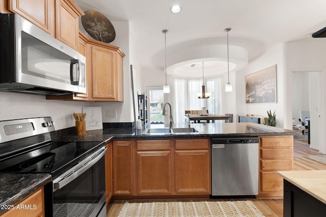 kitchen with appliances with stainless steel finishes, dark stone countertops, decorative light fixtures, a peninsula, and a sink