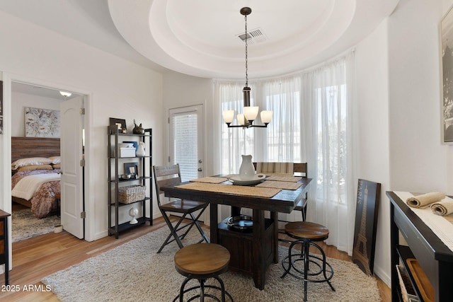 dining room featuring visible vents, baseboards, light wood-style floors, a tray ceiling, and an inviting chandelier