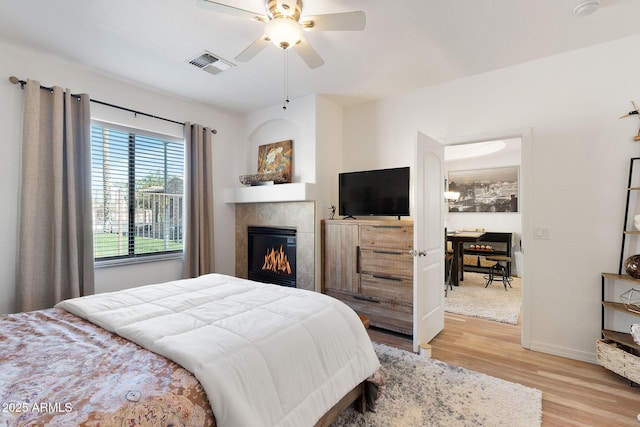 bedroom featuring ceiling fan, visible vents, baseboards, light wood-style floors, and a tiled fireplace