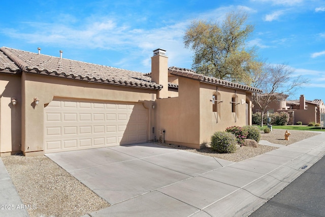 view of front of home with driveway, a chimney, a tiled roof, an attached garage, and stucco siding