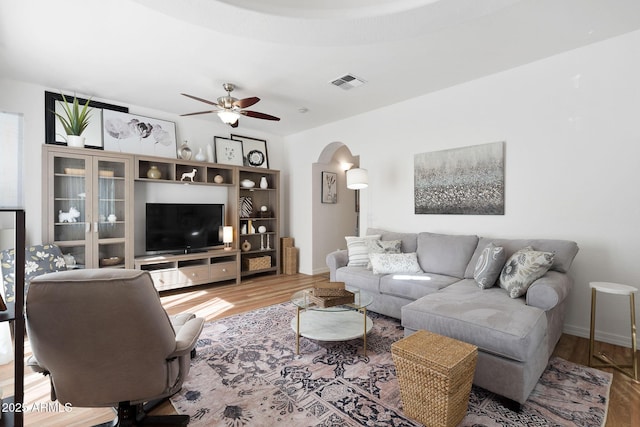 living room with arched walkways, visible vents, a ceiling fan, wood finished floors, and baseboards