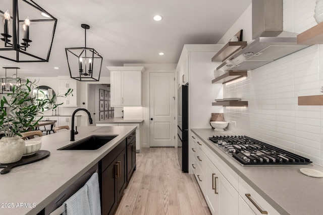 kitchen with sink, white cabinetry, hanging light fixtures, ventilation hood, and stainless steel gas cooktop