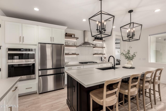 kitchen featuring white cabinetry, wall chimney exhaust hood, appliances with stainless steel finishes, and sink