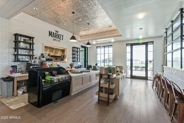 kitchen with hanging light fixtures, wood-type flooring, brick wall, and a raised ceiling