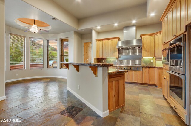 35824 N Tom Darlington Dr, Carefree, AZ 85377 - kitchen with wall chimney exhaust hood, baseboards, stone tile floors, stainless steel appliances, and recessed lighting