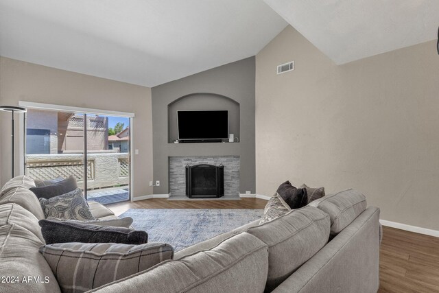 living room with lofted ceiling, hardwood / wood-style floors, and a stone fireplace