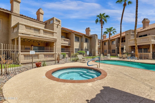 community pool with a hot tub, fence, and a patio