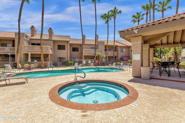 community pool with a patio area, fence, and a community hot tub