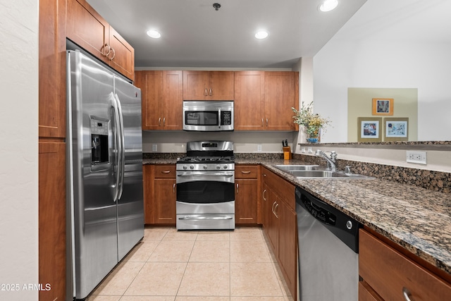 kitchen with appliances with stainless steel finishes, brown cabinetry, a sink, and light tile patterned floors