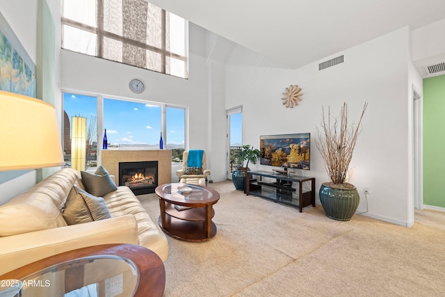 living room featuring carpet floors, a high ceiling, a glass covered fireplace, and visible vents