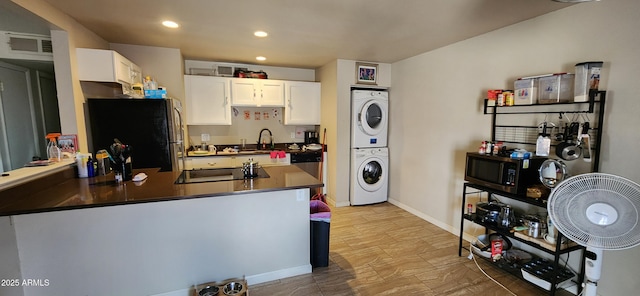 kitchen with freestanding refrigerator, stacked washer and clothes dryer, black electric stovetop, dark countertops, and white cabinetry