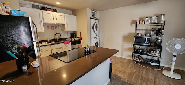 kitchen with stainless steel appliances, stacked washer / drying machine, dark countertops, a sink, and baseboards
