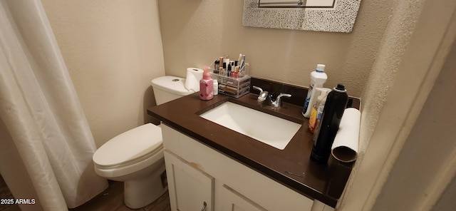 bathroom featuring a textured wall, toilet, and vanity