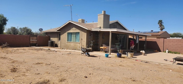 rear view of property with central air condition unit, fence, a gate, a chimney, and a patio area
