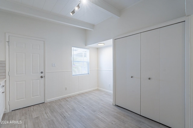 unfurnished bedroom with a closet, beam ceiling, a wainscoted wall, and light wood-style flooring