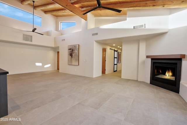 1637 N Quartz Valley Rd, Scottsdale, AZ 85266 - unfurnished living room with a wooden ceiling with exposed beams, ceiling fan, a warm lit fireplace, light tile patterned floors, and a high ceiling