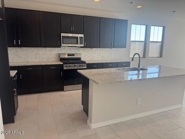 kitchen with light stone countertops, backsplash, stainless steel appliances, and a sink